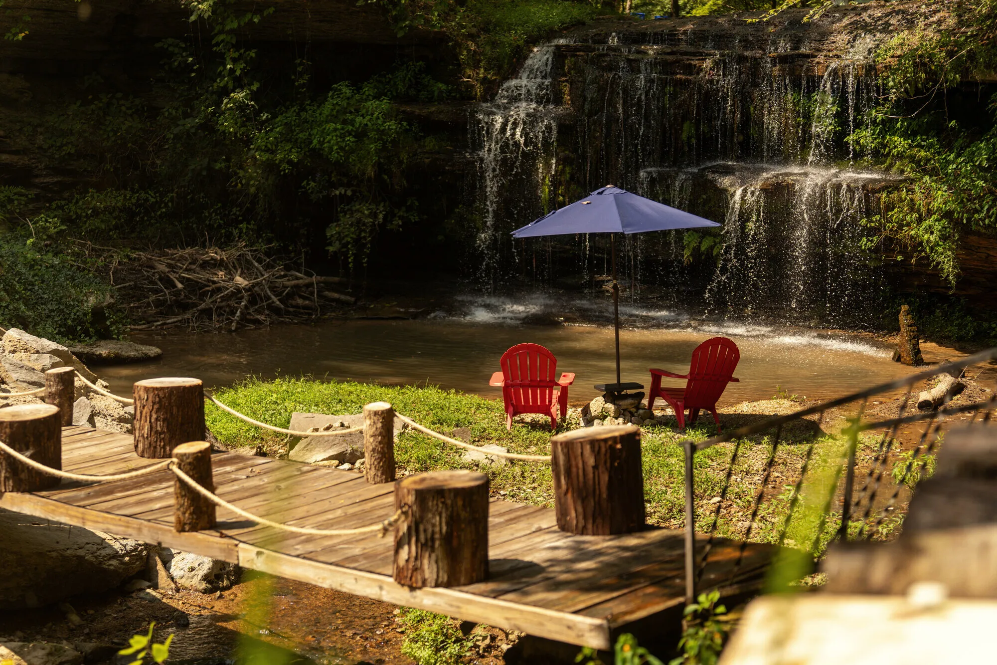 The plank boardwalk leading to two red Adirondack chairs and a blue umbrella at the foot of Old Falls
