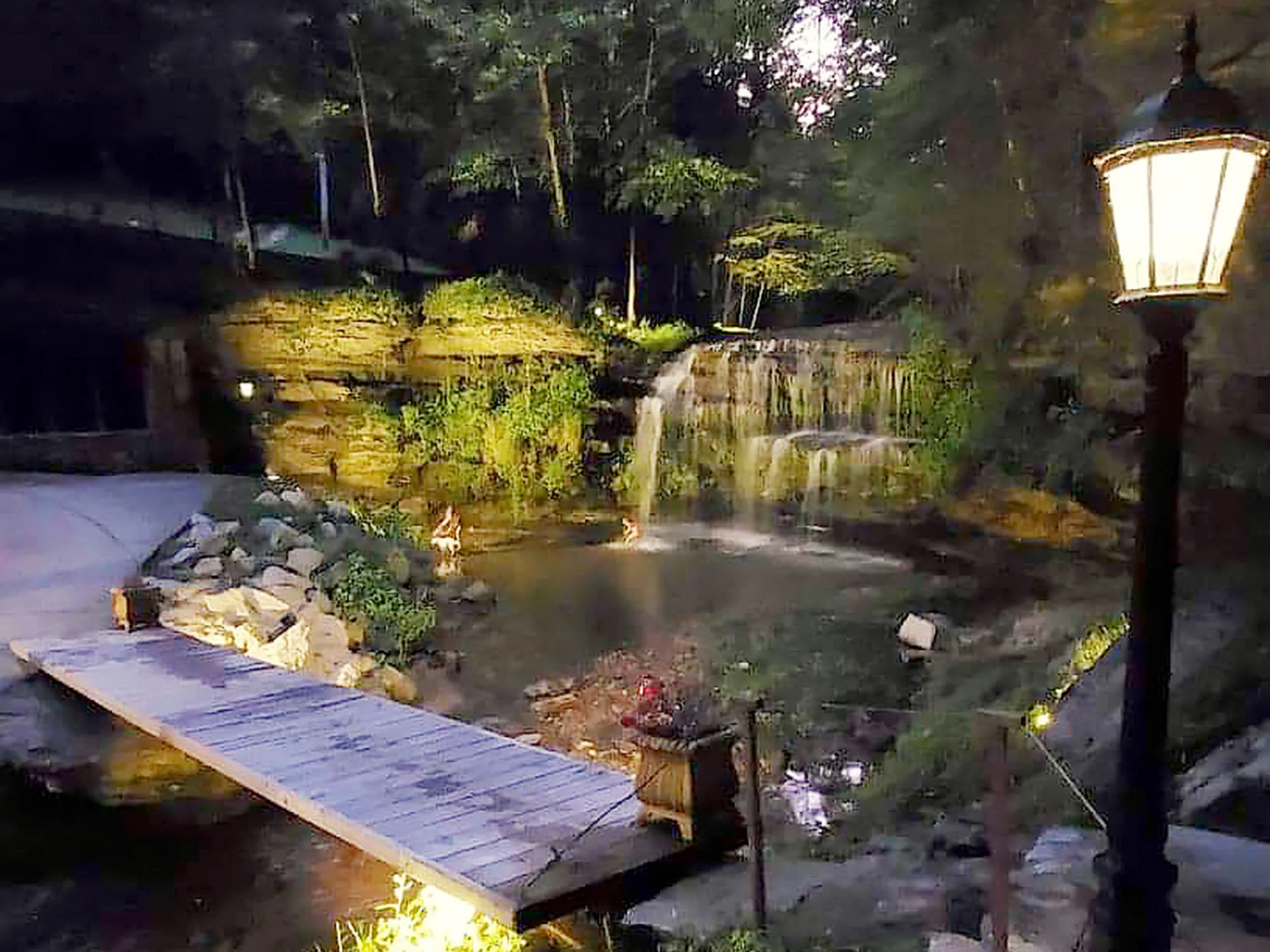 A wooden footbridge crossing Lick Creek directly beneath Old Falls, lit at dusk