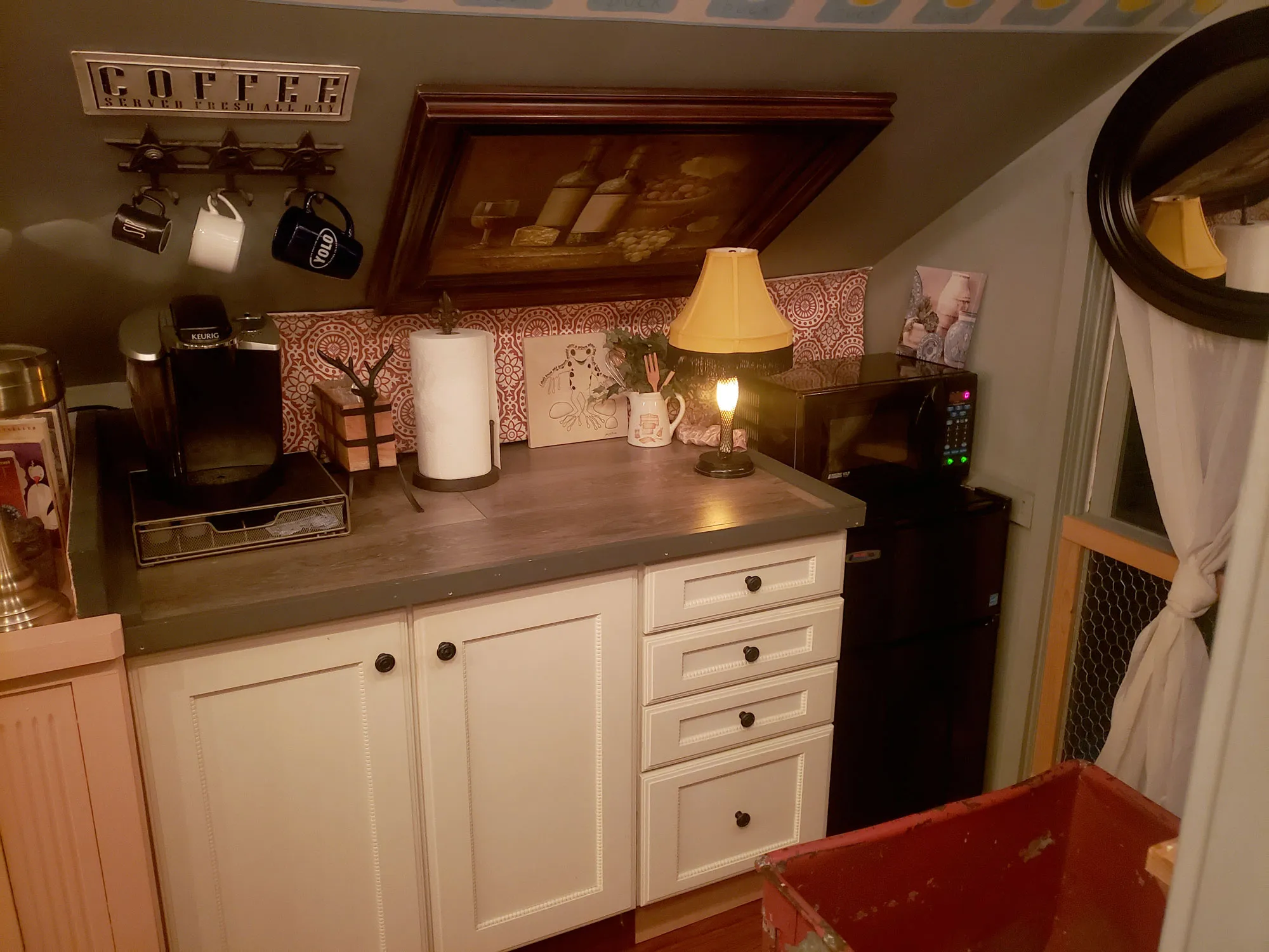 The kitchenette counter with a coffee maker, lamp, and framed art above it