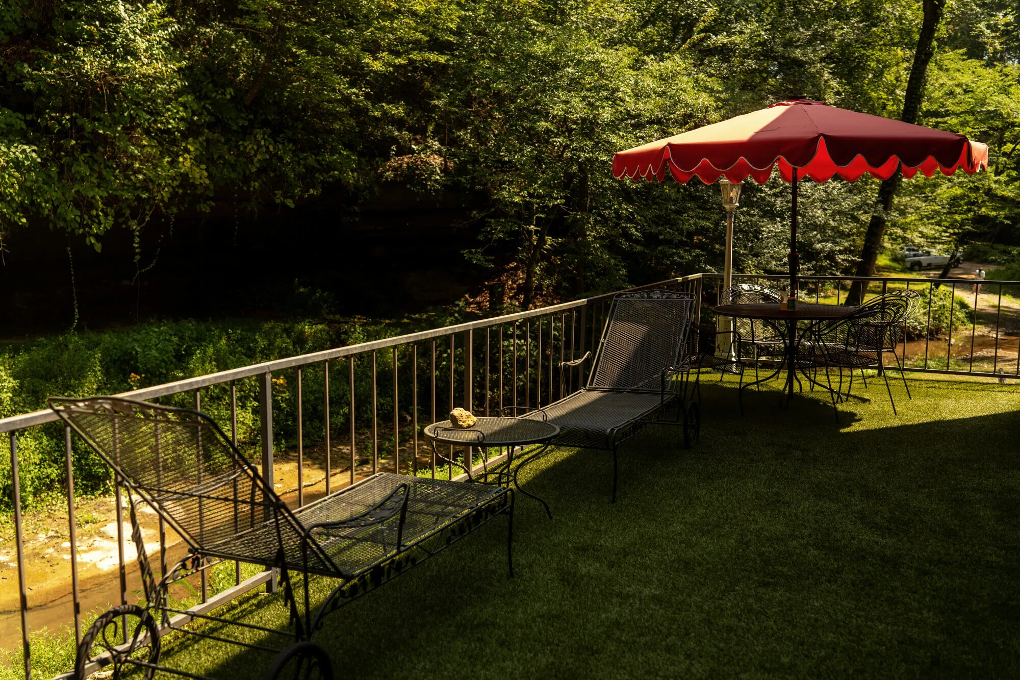 Wrought-iron loungers and a scalloped red umbrella on the green deck overlooking the creek