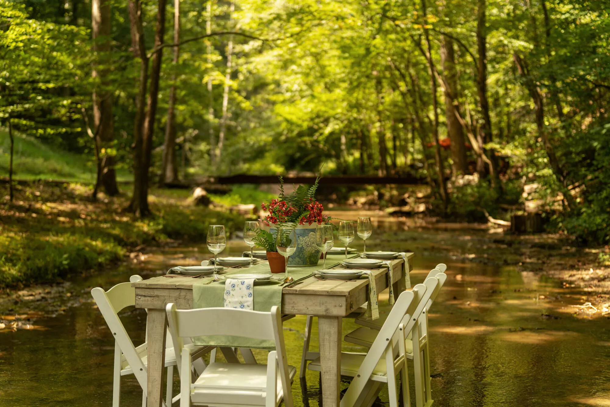 A long table set for dinner standing in the shallow creek, white chairs in the water on both sides