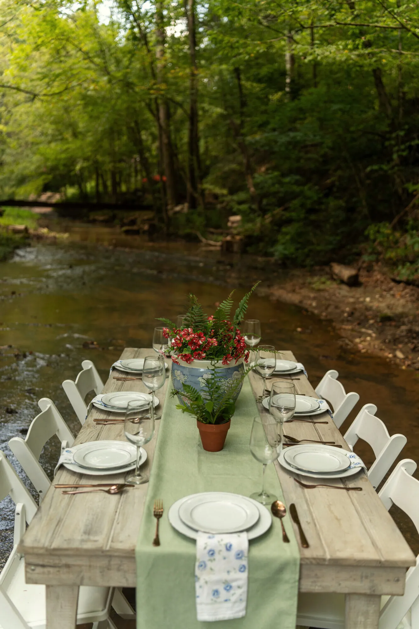 The dinner table seen end-on down the creek, place settings and a potted centerpiece running its length