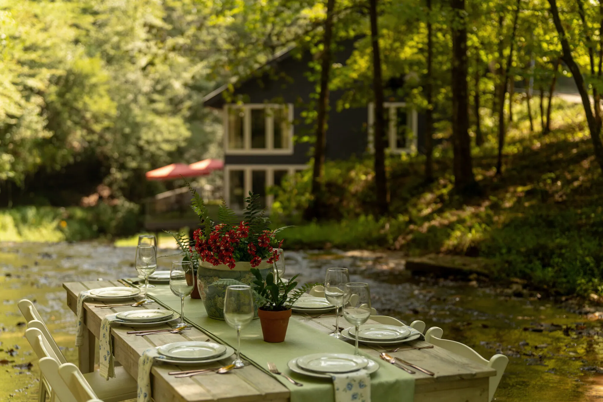 The laid dinner table in the creek with the Waterfall House and its red umbrella beyond the trees
