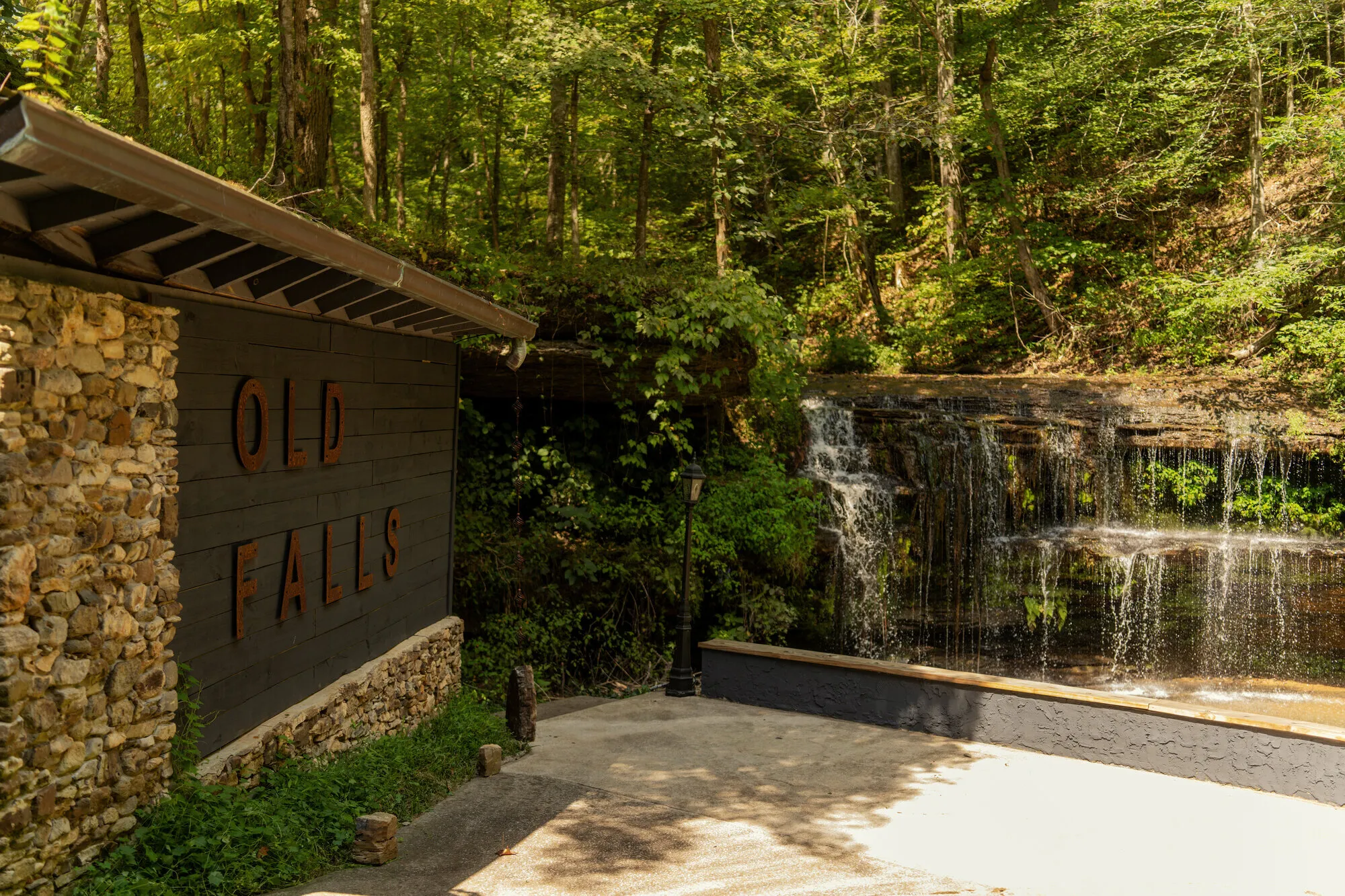 The stone-and-timber OLD FALLS sign standing beside the waterfall, its rusted steel letters catching the light