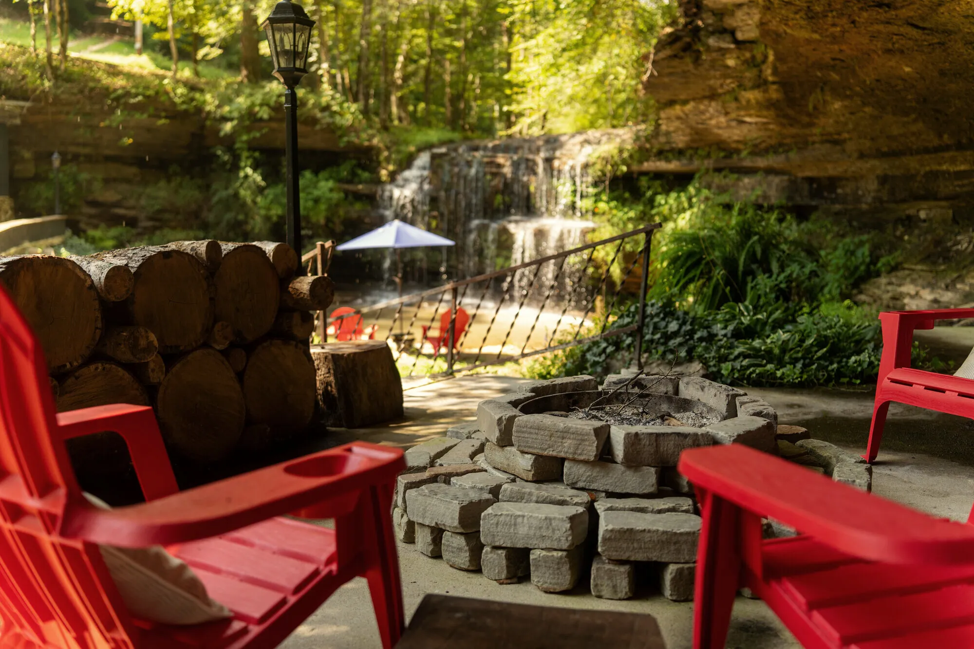 The stone fire pit ringed by red Adirondack chairs, the waterfall running behind it