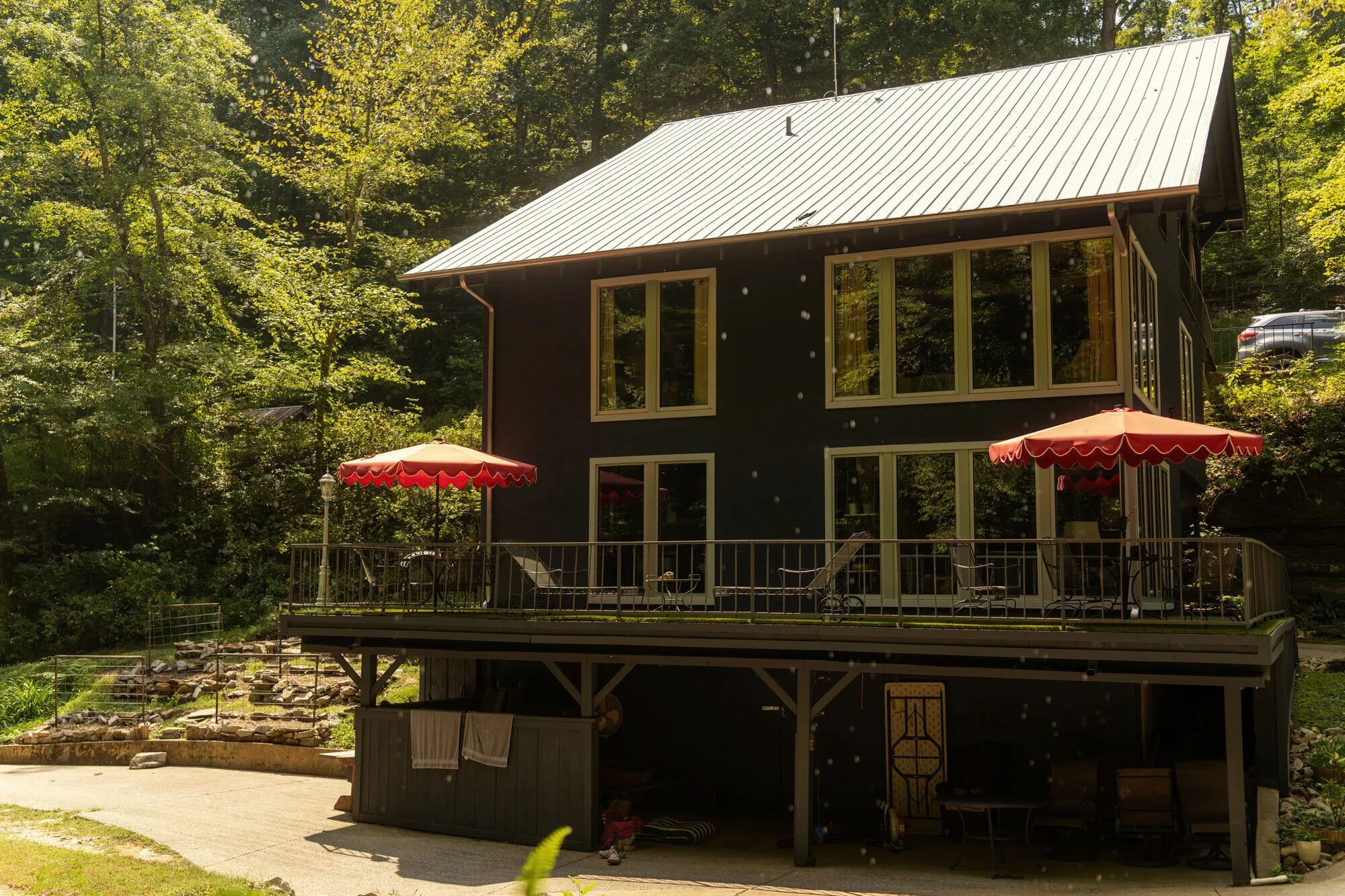 The dark-sided Waterfall House above its deck, red scalloped umbrellas open over the creek