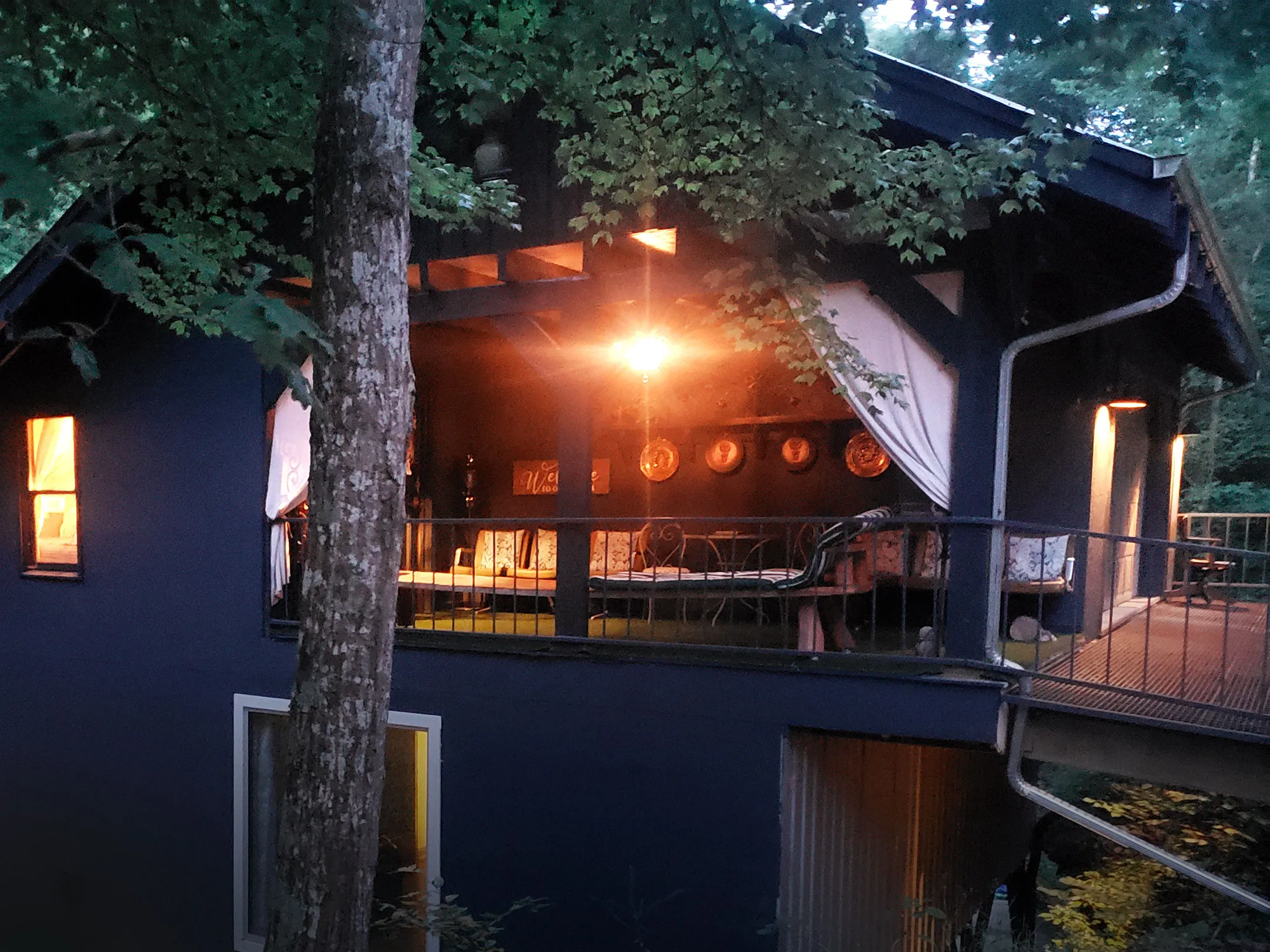 The upper deck of the Waterfall House at night, warm light spilling onto the boards
